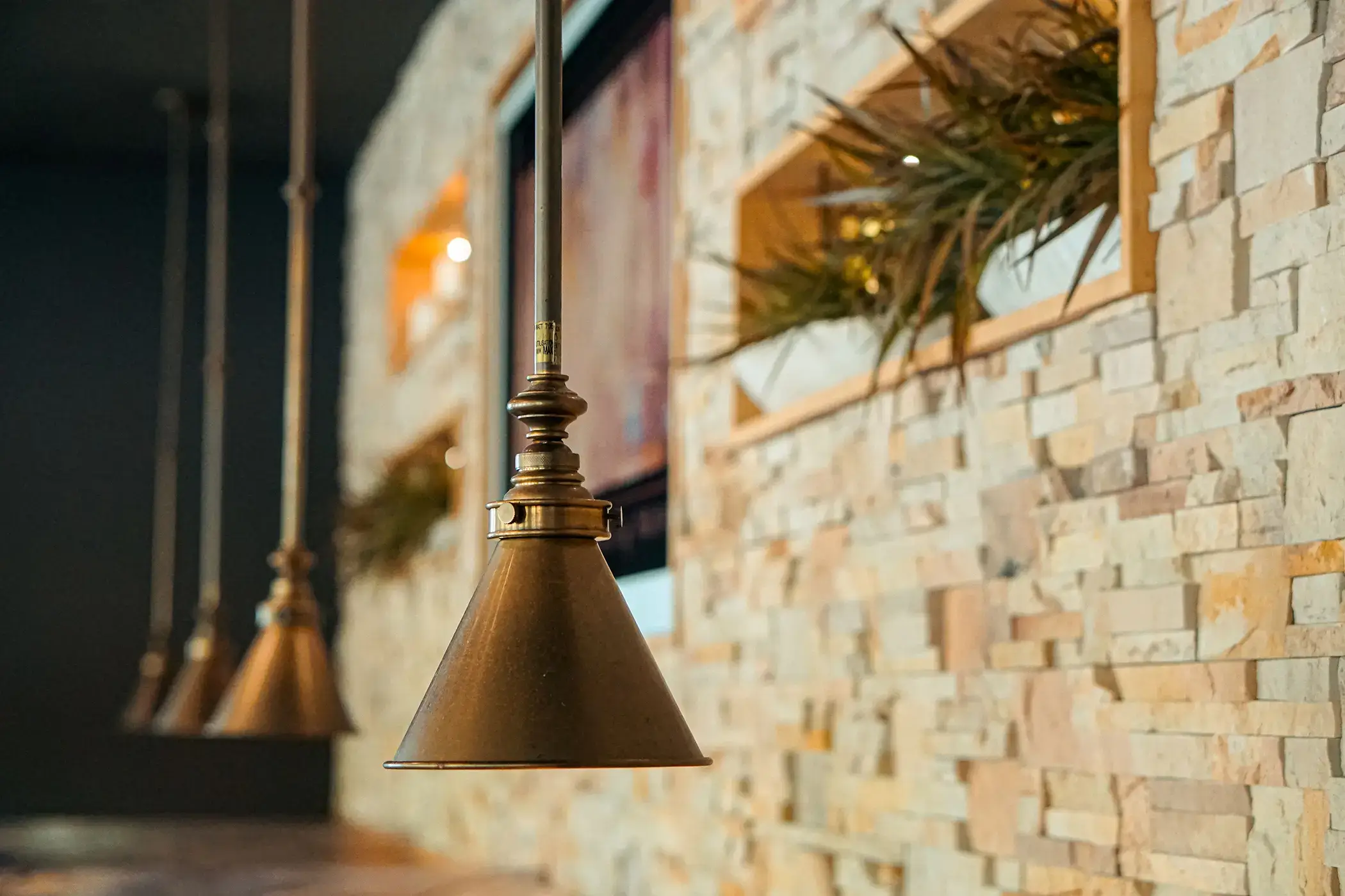rule prime pasta hanging copper lamps casting warm glow on textured stone wall closeup detail hickory nc
